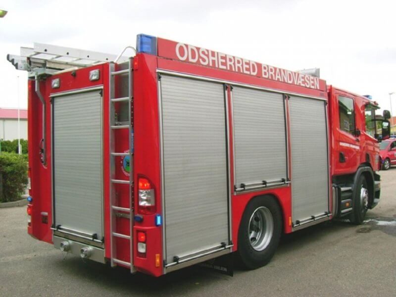 Rød brandbil fra Odsherred Brandvæsen parkeret på en asfalteret plads med stige på taget.